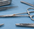 Stainless surgical instruments on a blue drape, one haemostat showing brown marking along the jaws and another instrument showing dark pitting